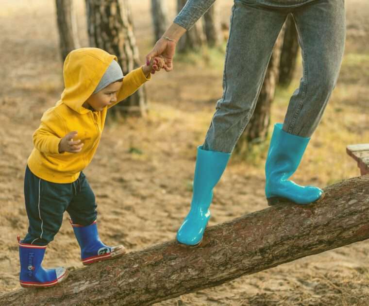 A balancing mother and child holding hands, walking up an angled log to tree house.