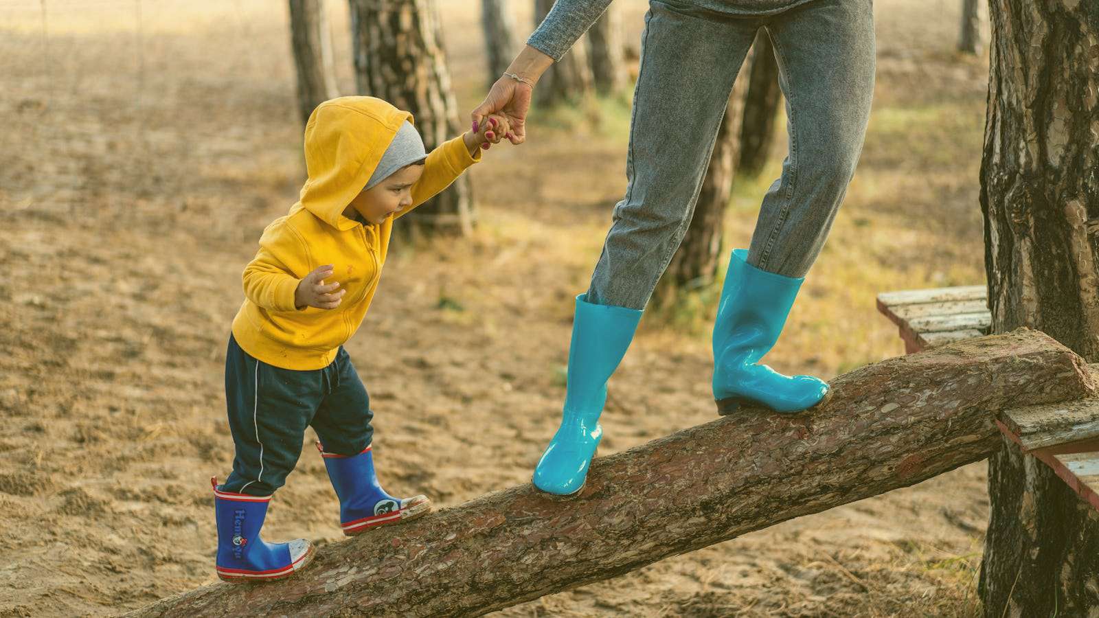A balancing mother and child holding hands, walking up an angled log to tree house.